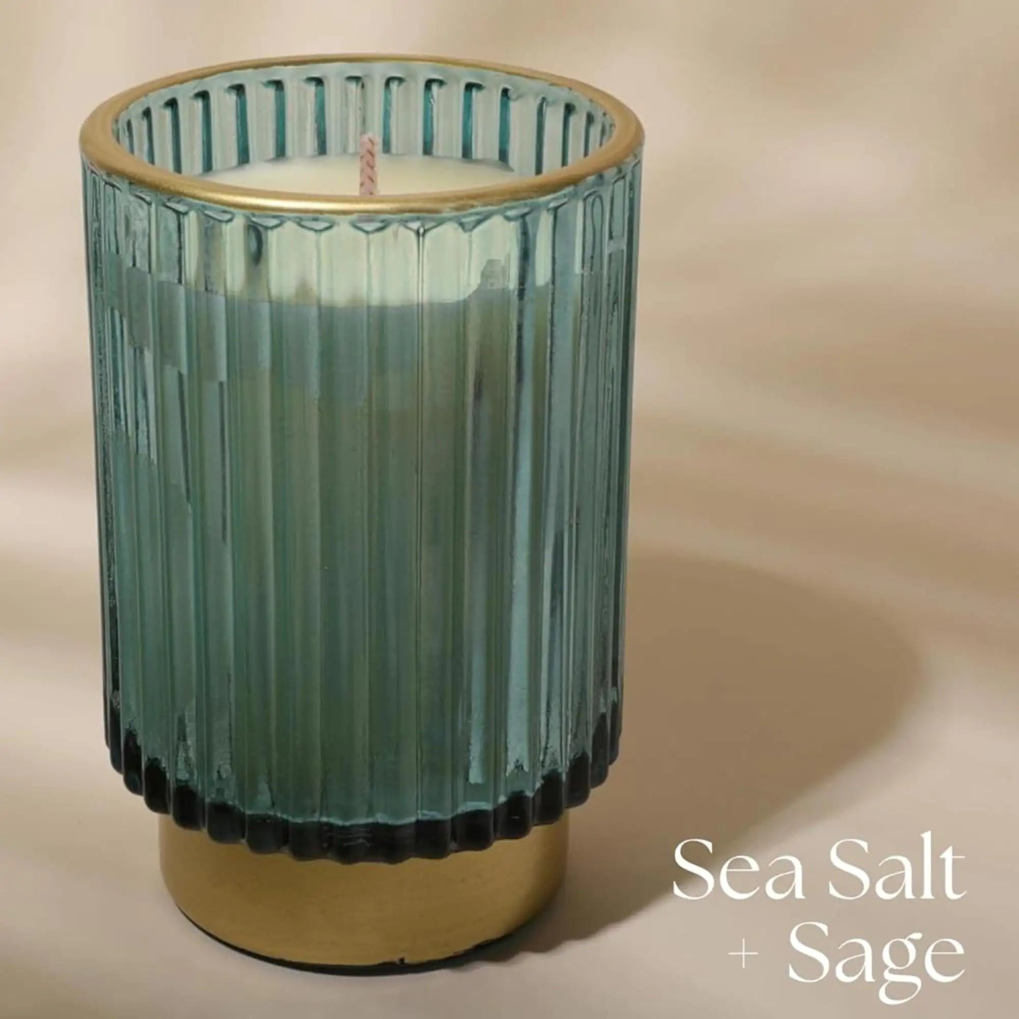 a glass candle holder with a gold rim and a sea salt and sage candle